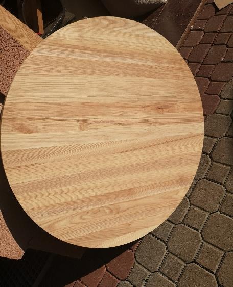 Okrągły blat z jasnego drewna dębowego, widoczne słoje, na tle kostki brukowej w odcieniach brązu i czerwieni.