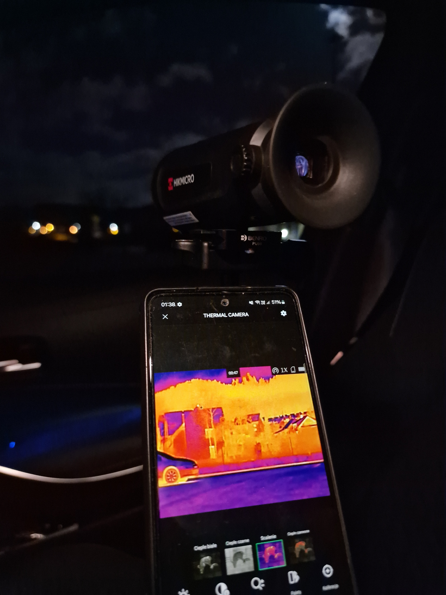 Kamera termowizyjna Hikmicro i smartfon z aplikacją termowizyjną, ukazujący obraz termiczny budynku i samochodu nocą. Sprzęt detektywistyczny w akcji.