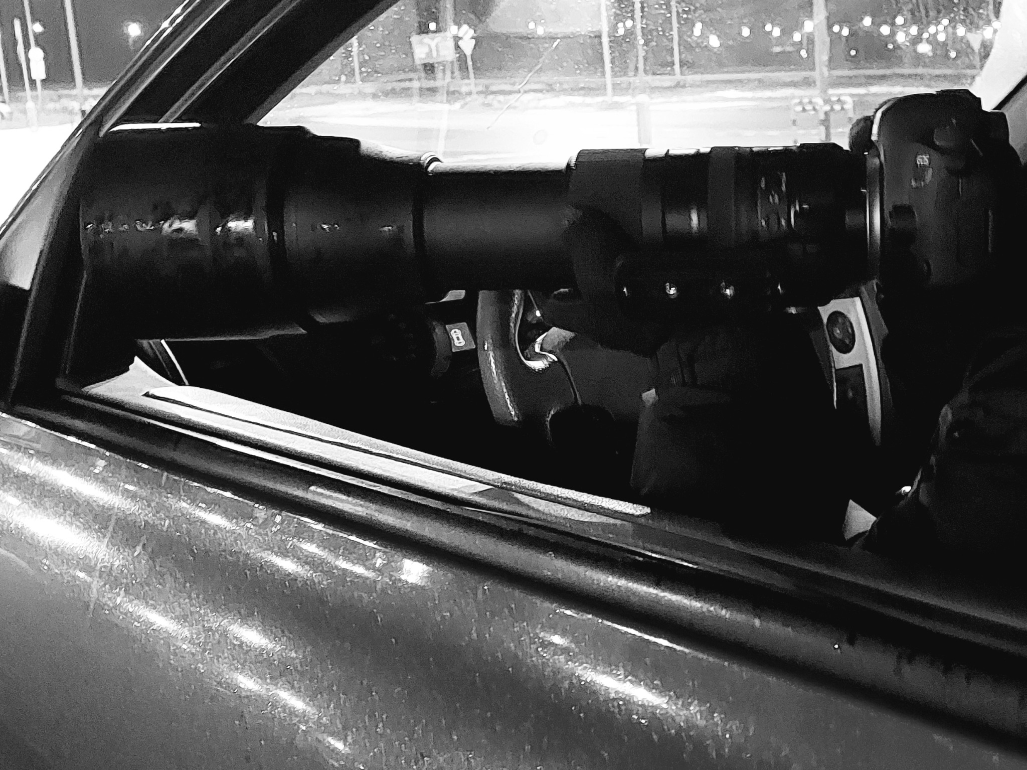 Długi teleobiektyw wystawiony przez okno samochodu, prawdopodobnie w celu obserwacji z ukrycia, widok nocny.