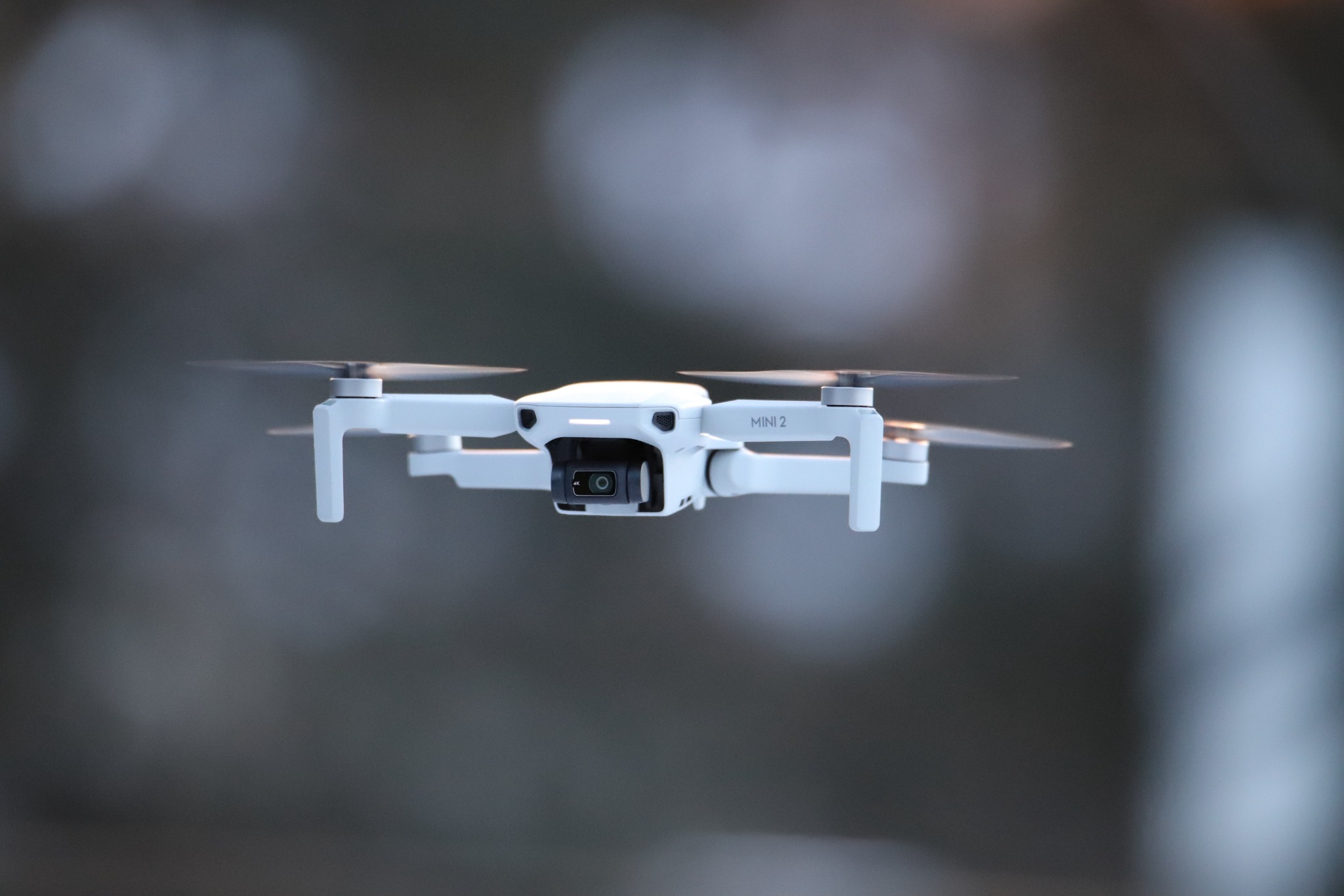 Biały dron Mini 2 w locie na rozmytym, szarym tle.