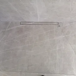 Ułożone szare płytki imitujące marmur z odpływem liniowym w kabinie prysznicowej, widoczne drobne niedociągnięcia montażowe.