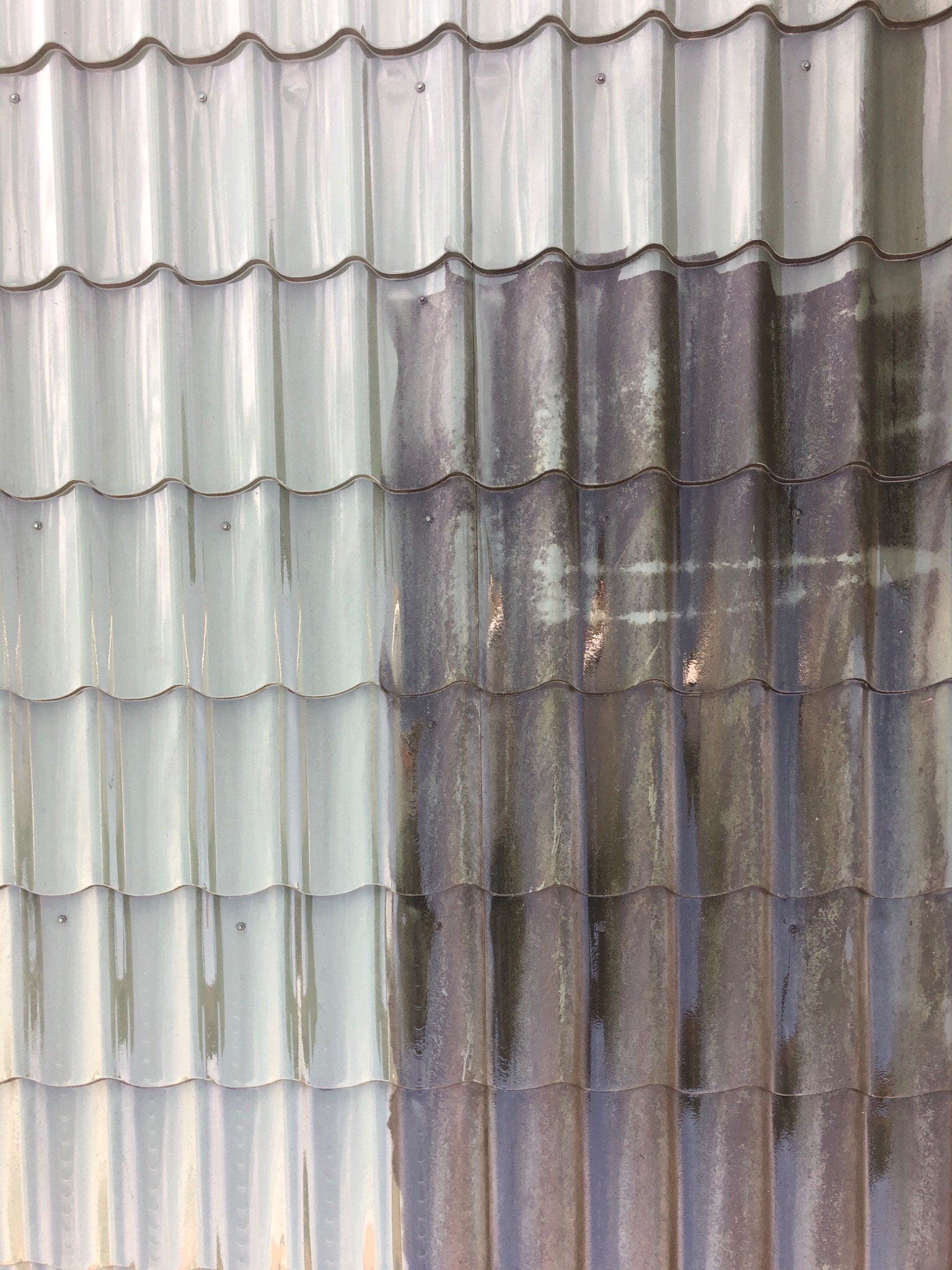 Częściowo umyty dach z szarej dachówki, ukazujący różnicę między czystą a brudną powierzchnią.