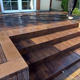 SELBRUK - Nowo ułożona kostka brukowa w odcieniach brązu i grafitu, tworząca schody wejściowe do domu, czyszczona myjką ciśnieniową, z widocznym efektem mokrej nawierzchni.