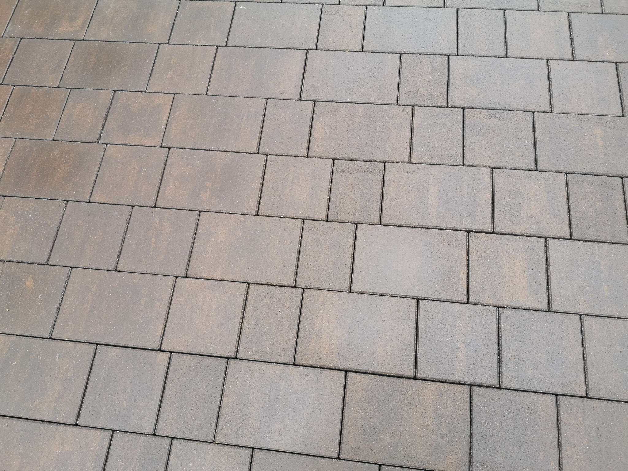 Ułożona, brązowo-szara kostka brukowa o prostokątnym kształcie, widoczna z perspektywy lekko z góry, z widocznymi fugami wypełnionymi piaskiem.