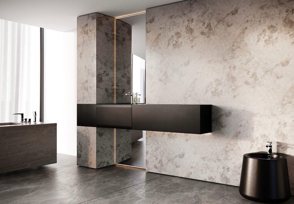 Minimalistyczna łazienka z ciemnoszarą, wiszącą szafką umywalkową, bidetem i ścianami o teksturze surowego betonu, oświetlenie LED akcentuje krawędzie lustra.