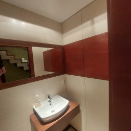 SkyProjects Bożena Wolińska - Nowoczesna umywalka nablatowa w łazience z beżowymi płytkami i drewnianymi akcentami, widok na lustro odbijające schody.