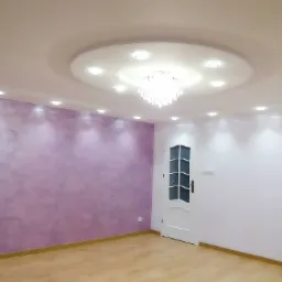 Wykończone wnętrze: ściana w odcieniach fioletu z efektem dekoracyjnym, drewniana podłoga, białe ściany z halogenami i ozdobny sufit z żyrandolem, białe drzwi z szybami.