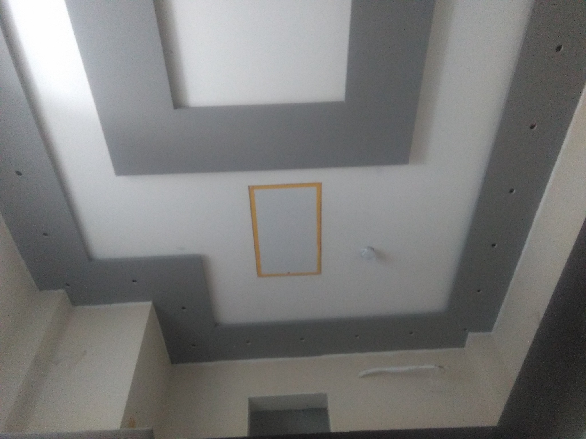 Dekoracyjny sufit podwieszany z szarymi elementami i prostokątnym otworem w centralnej części, oświetlenie punktowe wzdłuż krawędzi.