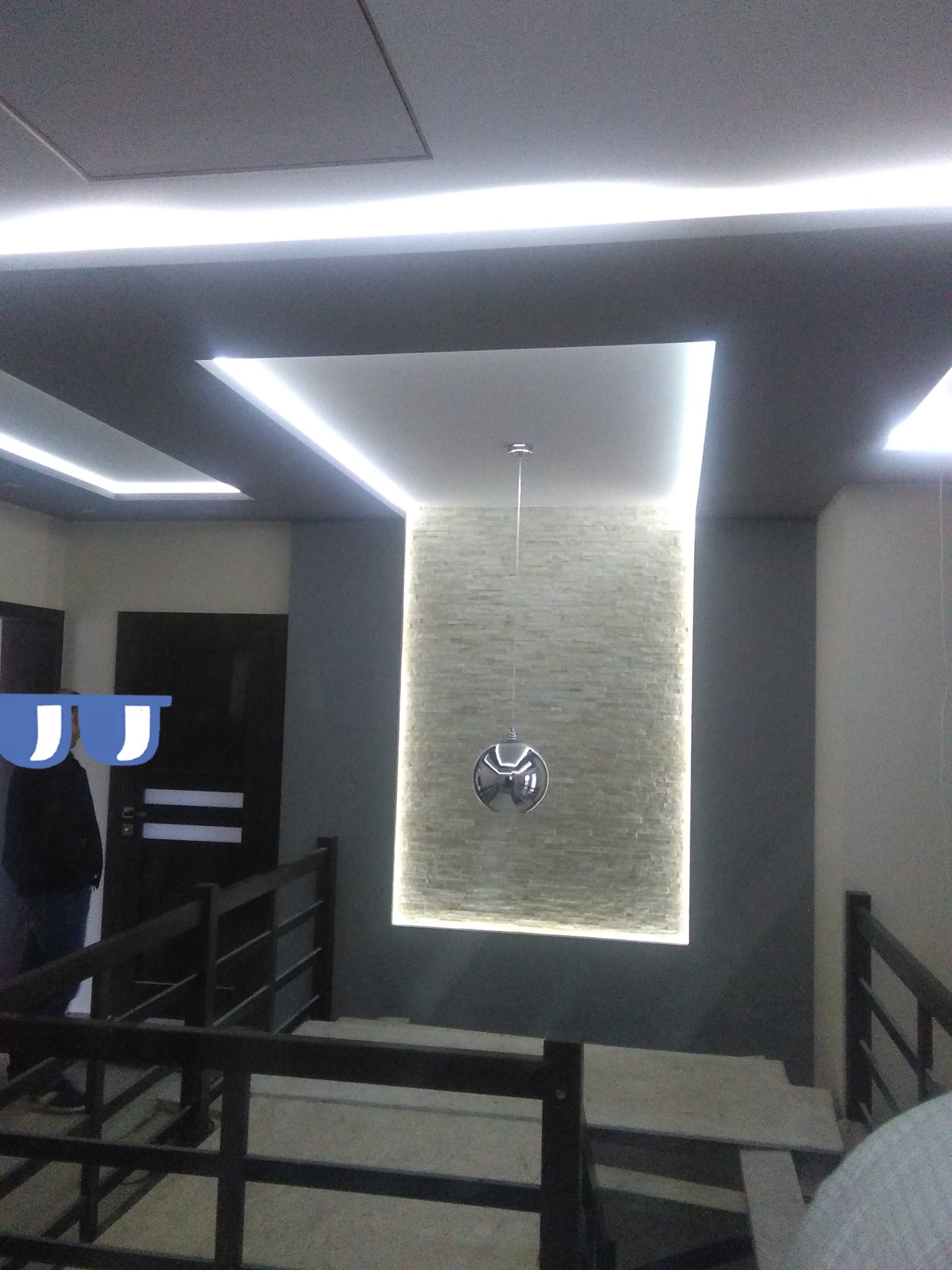 Nowoczesny sufit z oświetleniem LED, fragment ściany z dekoracyjną okładziną imitującą kamień, widok z klatki schodowej.