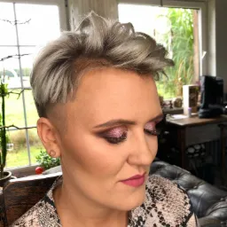 Kobieta z platynowymi włosami i intensywnym, różowym cieniem na powiekach oraz matową pomadką w odcieniu maliny, pozująca w pomieszczeniu z oknami.