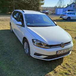 Biały samoch&oacute;d kombi na trawiastym terenie, z widocznym numerem rejestracyjnym SPS 89701 i innymi pojazdami w tle.