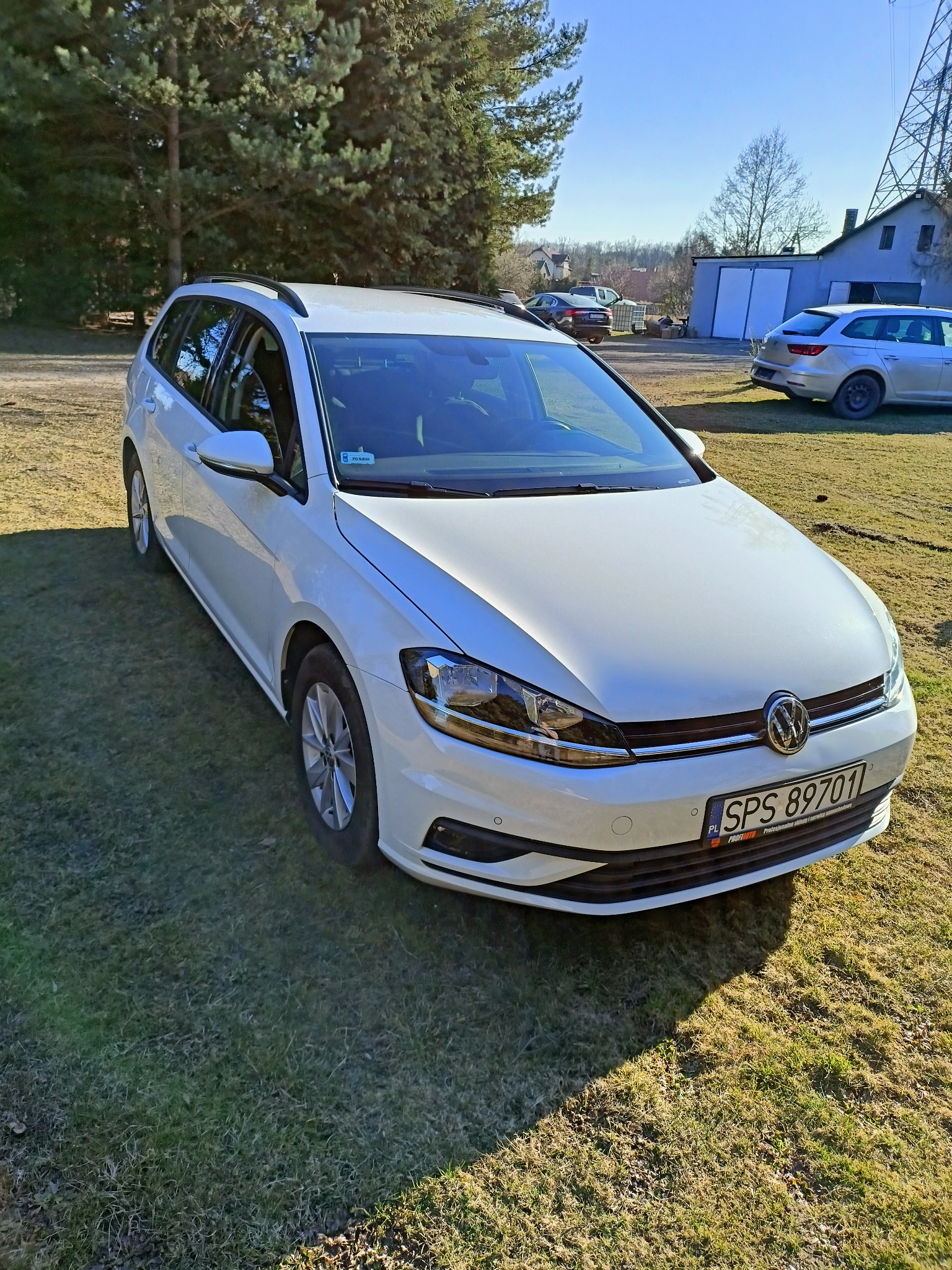 Biały samochód kombi na trawiastym terenie, z widocznym numerem rejestracyjnym SPS 89701 i innymi pojazdami w tle.