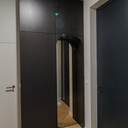 AWENAmeble - Nowoczesna, czarna szafa wnękowa z lustrem w kształcie łuku, wkomponowana w przedpokój z parkietem w jodełkę i surowym betonowym sufitem.