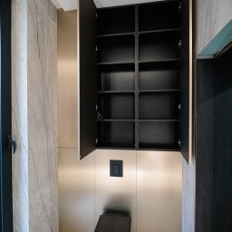 AWENAmeble - Nowoczesna łazienka z zabudową meblową: szafka wnękowa nad toaletą, fronty w kolorze beżowego złota, wnętrze szafki czarne z półkami, marmurowe płytki na ścianach i podłodze.