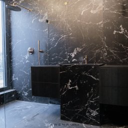 AWENAmeble - Nowoczesna łazienka z czarnymi szafkami pod umywalką i ścianami wyłożonymi czarnym marmurem z białymi żyłami, widoczny deszczownica i okno z widokiem na zewnątrz.