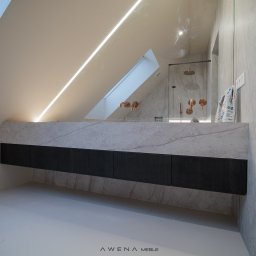 AWENAmeble - Nowoczesna łazienka na poddaszu ze skośnym sufitem i oknem dachowym, marmurowy blat z szafkami w kolorze ciemnego drewna, miedziana armatura i kabina prysznicowa w tle.