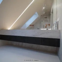 Nowoczesna łazienka na poddaszu ze skośnym sufitem i oknem dachowym, marmurowy blat z szafkami w kolorze ciemnego drewna, miedziana armatura i kabina prysznicowa w tle.