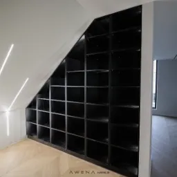 Czarna, zabudowana półka w skosie poddasza, z oświetleniem LED na ścianie i parkietem w jodełkę, widok z boku.