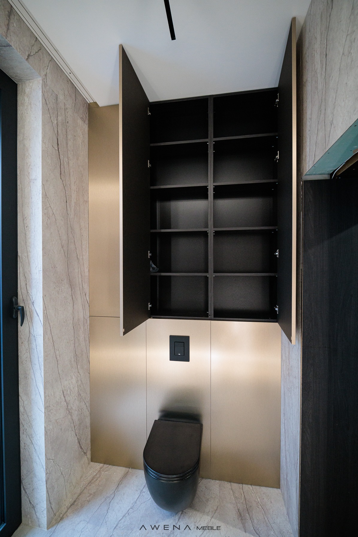 Nowoczesna łazienka z zabudową meblową: szafka wnękowa nad toaletą, fronty w kolorze beżowego złota, wnętrze szafki czarne z półkami, marmurowe płytki na ścianach i podłodze.