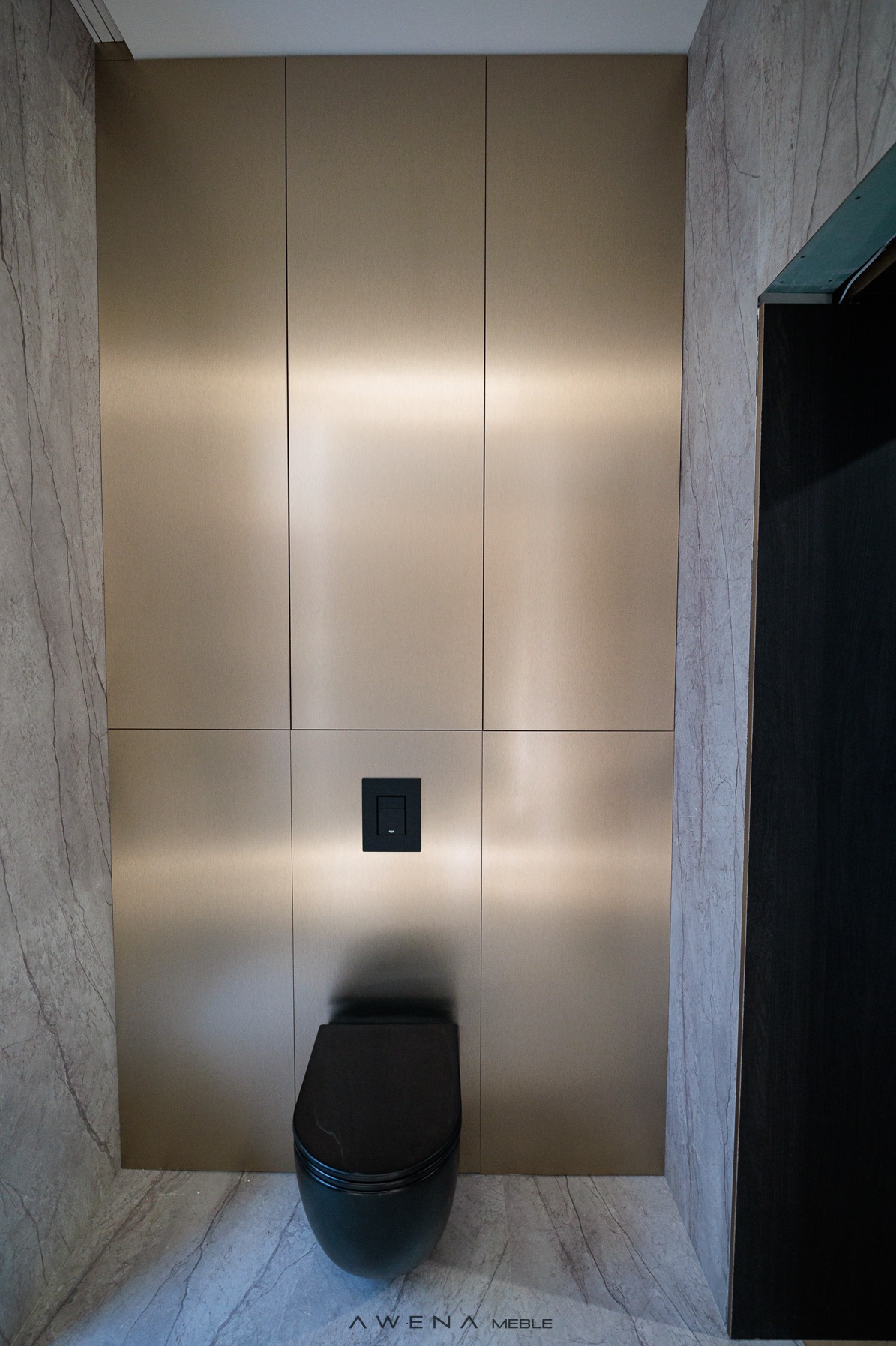 Nowoczesna toaleta podwieszana w zabudowie z paneli w odcieniach złota, z czarnym przyciskiem spłukującym i marmurową okładziną ściany.