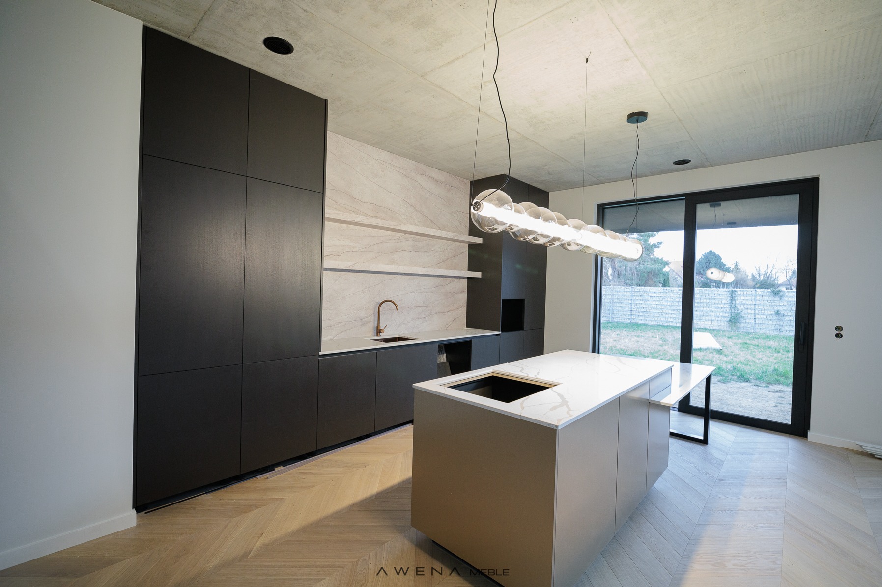 Nowoczesna kuchnia w Radomsku z ciemnymi szafkami, marmurowym backsplashiem i wyspą kuchenną z jasnym blatem, oświetlona designerską lampą wiszącą.
