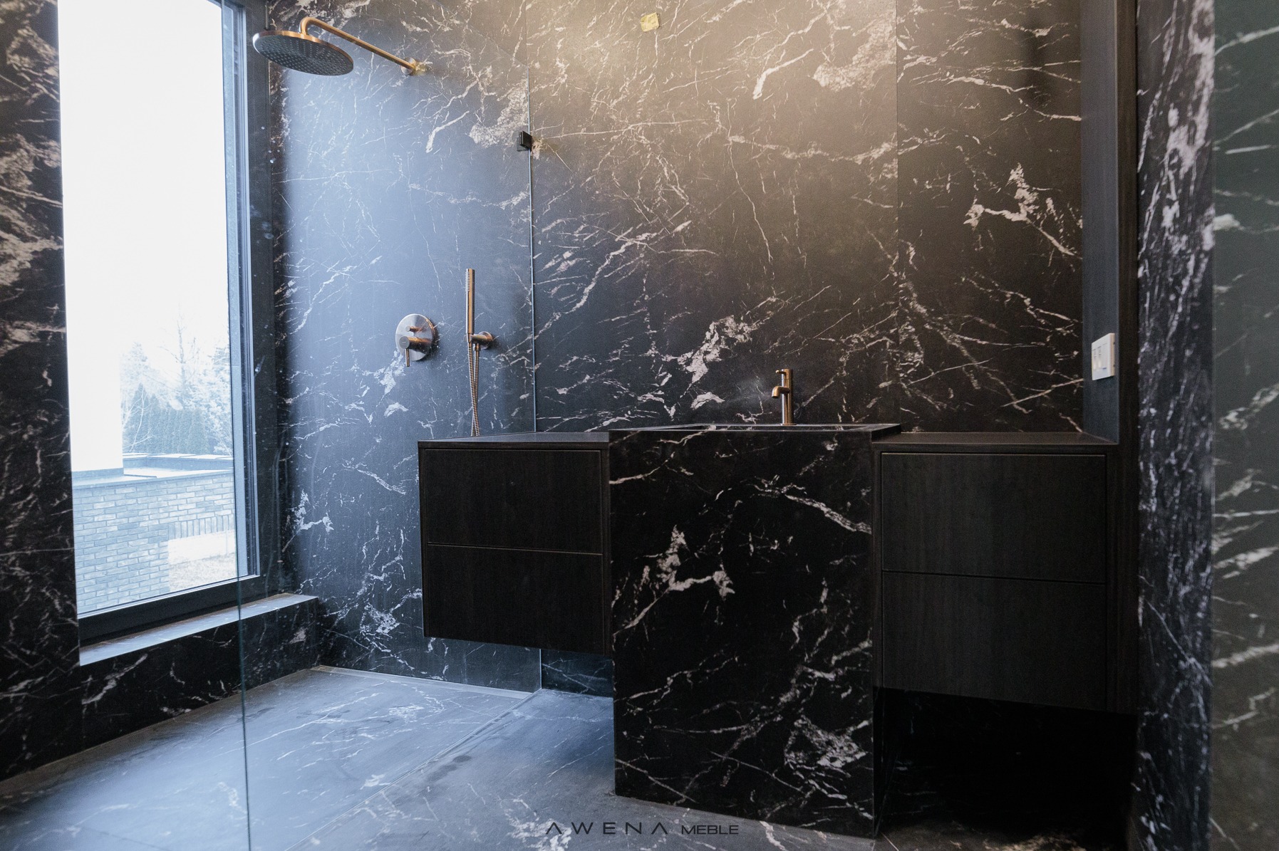 Nowoczesna łazienka z czarnymi szafkami pod umywalką i ścianami wyłożonymi czarnym marmurem z białymi żyłami, widoczny deszczownica i okno z widokiem na zewnątrz.