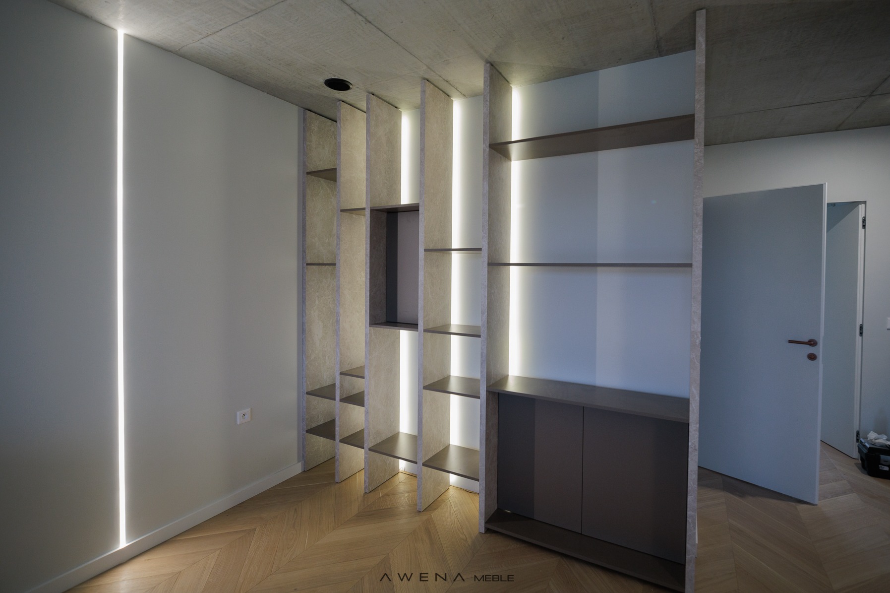 Nowoczesna szafa wnękowa z podświetleniem LED, betonowy sufit i parkiet w jodełkę, widok na otwarte drzwi.