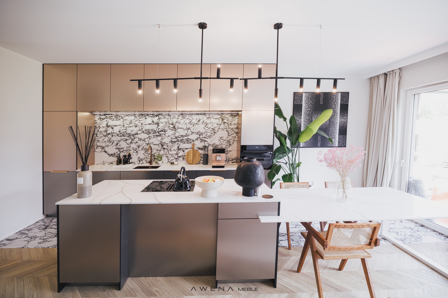 Nowoczesna kuchnia z wyspą, marmurowym backsplashiem i podłogą w jodełkę, oświetlona czarną lampą sufitową, z elementami dekoracyjnymi i roślinami.