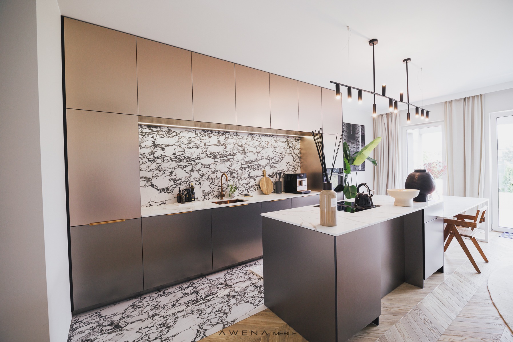 Nowoczesna kuchnia z wyspą, fronty szafek w kolorze taupe, marmurowy backsplash i podłoga, minimalistyczne oświetlenie wiszące, ekspres do kawy na blacie.