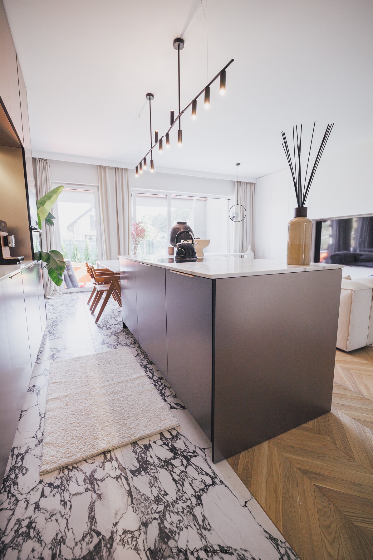 Nowoczesna kuchnia z wyspą, marmurową podłogą i drewnianym parkietem, oświetlenie punktowe, minimalistyczny design, czajnik na blacie.