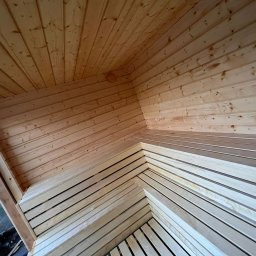 EKO SZKIELET SPÓŁKA Z OGRANICZONĄ ODPOWIEDZIALNOŚCIĄ - Wnętrze konstrukcji z jasnego drewna, widoczne deski na ścianach i suficie, częściowo wykończone siedzisko w rogu, okno z widokiem na zieleń na zewnątrz.