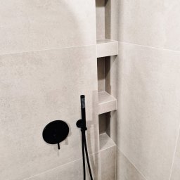 REMKOR - Minimalistyczna kabina prysznicowa z beżowymi płytkami i czarną armaturą, wnęki w ścianie. Nowoczesny design, stonowana kolorystyka, precyzyjne wykończenie.