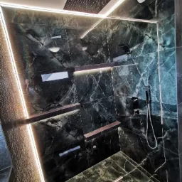 Elegancka kabina prysznicowa z marmurowymi płytkami w odcieniach zieleni, podświetlona listwami LED, z deszczownicą i półkami wkomponowanymi w ścianę.