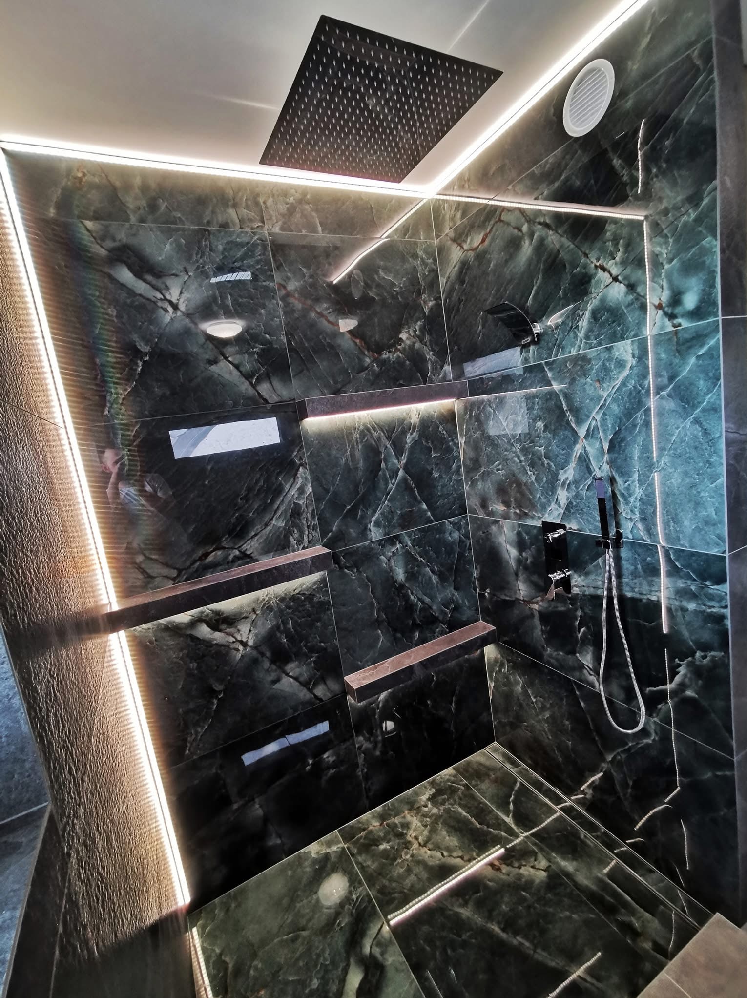 Elegancka kabina prysznicowa z marmurowymi płytkami w odcieniach zieleni, podświetlona listwami LED, z deszczownicą i półkami wkomponowanymi w ścianę.