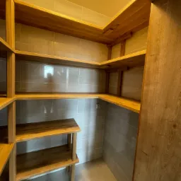 Drewniane półki spiżarni na wymiar z szarymi płytkami na ścianach, oświetlone górnym światłem.