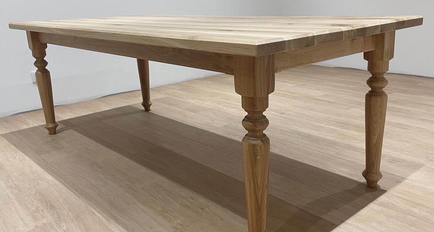 Stół z jasnego drewna z toczonymi nogami w stylu rustykalnym, widoczny na tle drewnianej podłogi i jasnej ściany.