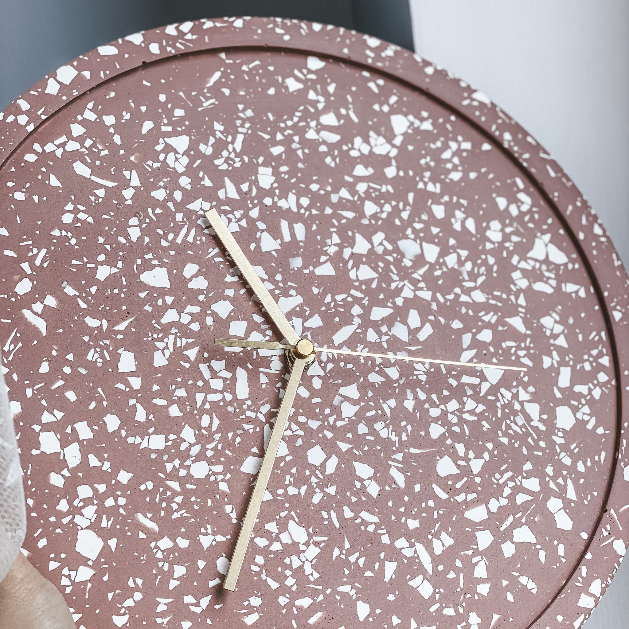 Okrągły zegar ścienny w kolorze terakoty z białym wzorem lastryko i złotymi wskazówkami.