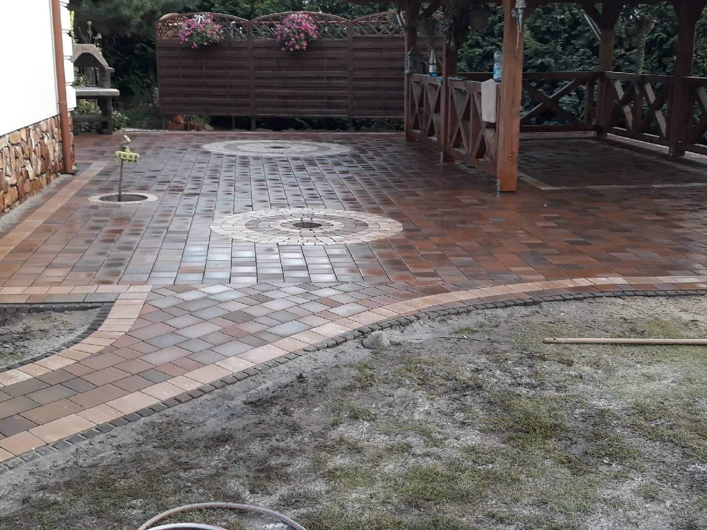 Wykończony podjazd z kostki brukowej w Bydgoszczy, z dekoracyjnymi okręgami z jaśniejszej kostki i zadaszeniem altany w tle.
