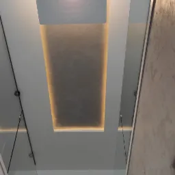 Nowoczesne wnętrze klatki schodowej z oświetleniem LED w suficie, szklane balustrady i dekoracyjna donica z roślinami na podeście.