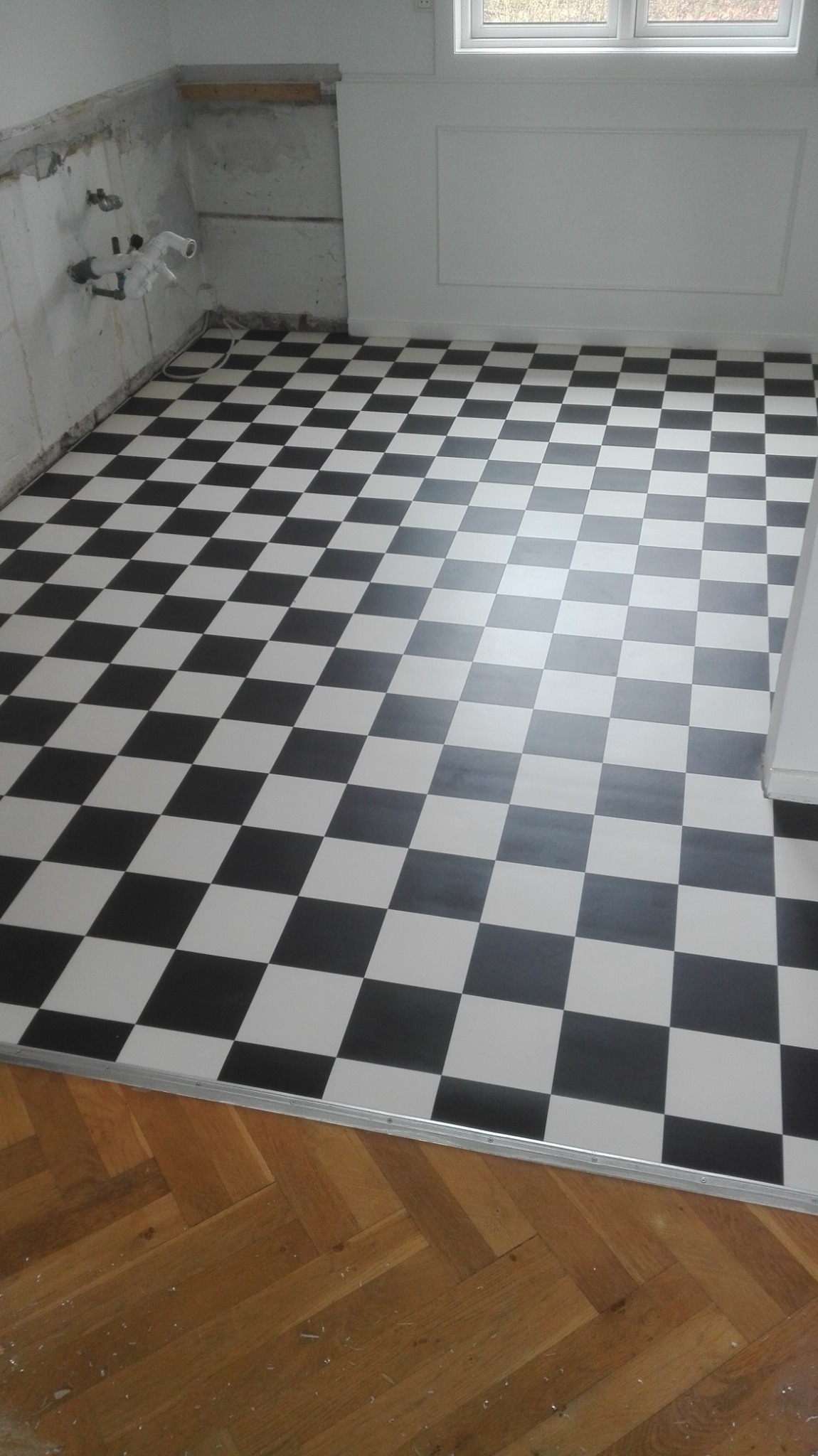 Wnętrze w trakcie prac: położona szachownica z czarno-białych płytek podłogowych, widoczne przygotowane ściany i fragment drewnianego parkietu.