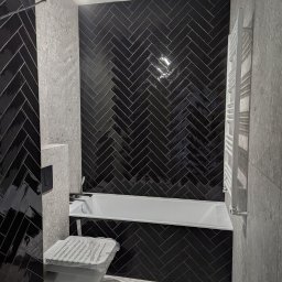 Quick Refit Daniel Rychlewski - Ciemna łazienka w jodełkę: czarne, błyszczące płytki na ścianie za wanną, szare płytki na ścianie bocznej i podłodze. Biała wanna i grzejnik.