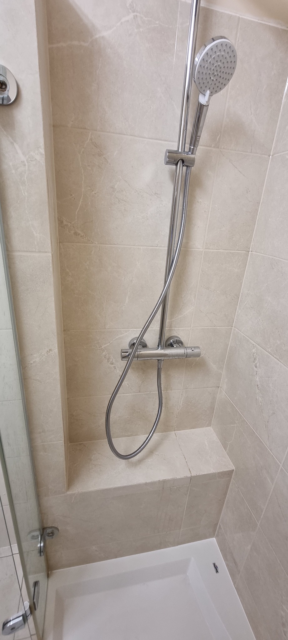 Kabina prysznicowa z deszczownicą i termostatem, wykończona beżowymi płytkami imitującymi marmur, widoczny fragment szklanych drzwi.