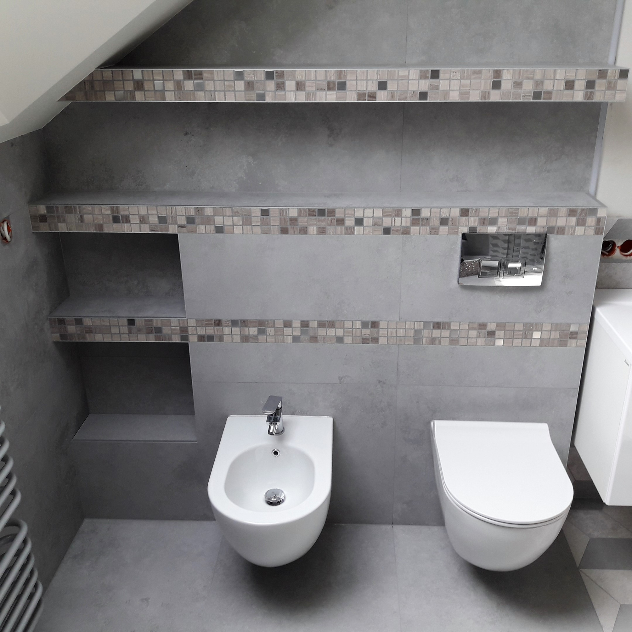 Nowoczesna łazienka w szarościach z mozaiką, wisząca toaleta i bidet, półki wnękowe z podświetleniem.