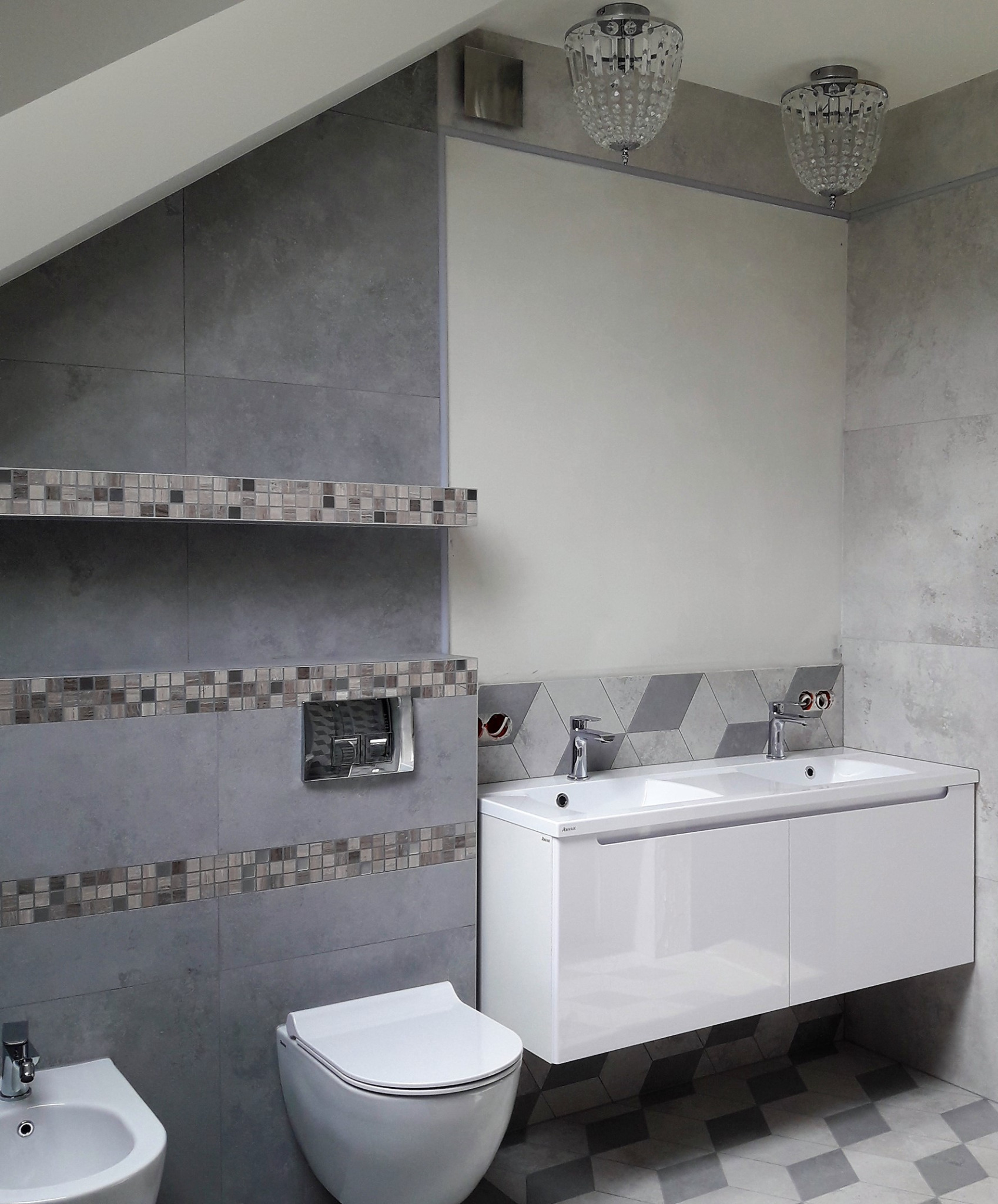 Nowoczesna łazienka z szarymi płytkami, mozaikowymi akcentami, podwieszaną toaletą, bidetem i podwójną umywalką z białą szafką, podświetlona ozdobnymi lampami sufitowymi.