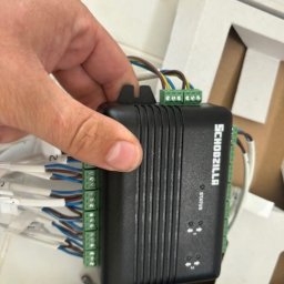 Electro-Stach Janusz Stachura - Czarny moduł sterujący Schodzilla z podłączonymi przewodami, trzymany w dłoni, widoczne złącza śrubowe i diody statusu.