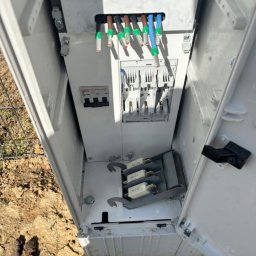 Electro-Stach Janusz Stachura - Otwarta skrzynka elektryczna z widocznymi przewodami, bezpiecznikami i elementami złącznymi, umieszczona na ziemi.