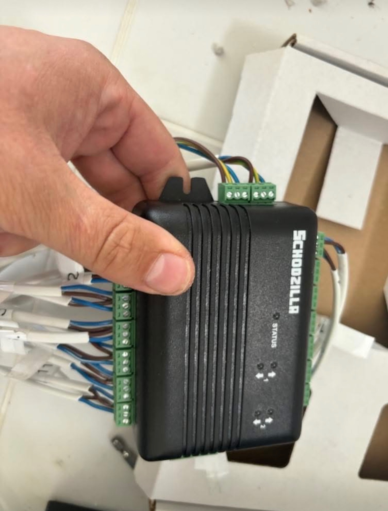 Czarny moduł sterujący Schodzilla z podłączonymi przewodami, trzymany w dłoni, widoczne złącza śrubowe i diody statusu.