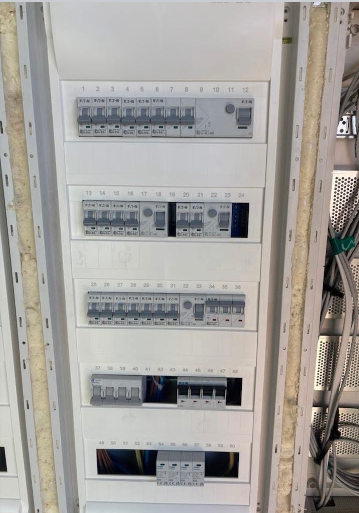 Rozdzielnica elektryczna z bezpiecznikami, widoczne numery od 1 do 60, przewody w korytku kablowym po prawej stronie.