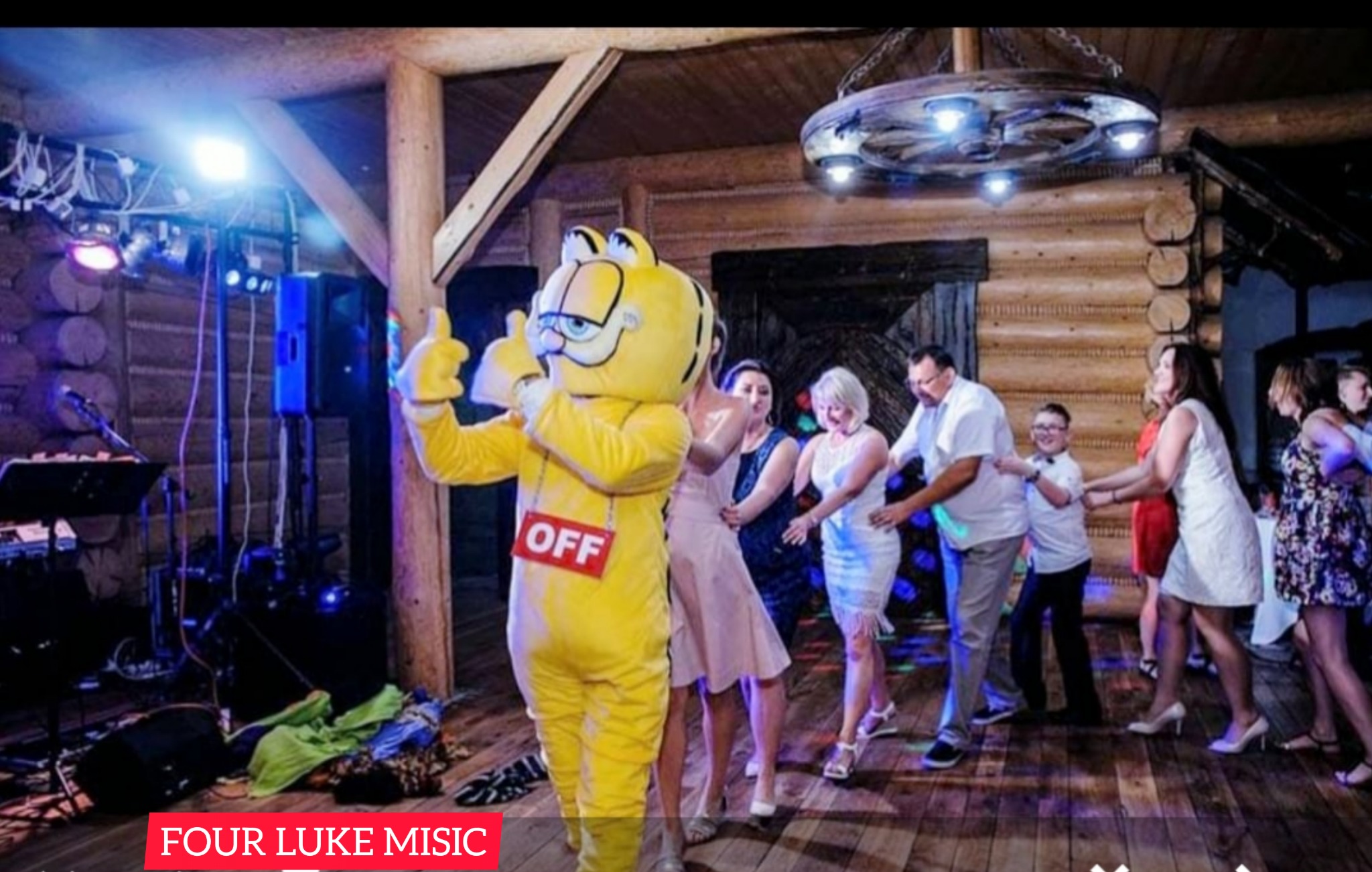 Osoba w kostiumie Garfielda z napisem 'OFF' na czerwonej tabliczce, tańcząca z gośćmi na drewnianym parkiecie w rustykalnym wnętrzu podczas imprezy, w tle sprzęt muzyczny i oświetlenie sceniczne.