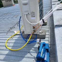 Montaż zewnętrznej jednostki klimatyzacji GREE na blaszanym dachu, widoczne przewody chłodnicze, pompa próżniowa i węże serwisowe.